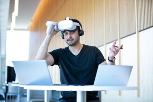 Dr. Peyman Yousefi teaching an online class via Zoom and exploring virtual watershed for flood management strategies. He is wearing a Virtual Reality headset while sitting in front of two laptops.